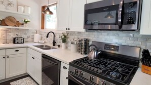 A modern kitchen with white cabinets, a stainless steel stove, a microwave, and a sink. - Coal Creek Cottage (hot tub, dog and kid friendly) (Sedro-Woolley)