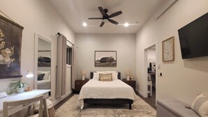 A bedroom with a bed, bedside tables, a desk, a chair, a ceiling fan, and a TV on the wall. - Coal Creek Cottage (hot tub, dog and kid friendly) (Sedro-Woolley)