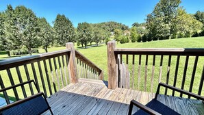 Una terraza de madera con dos sillas y vista a un área verde con árboles.