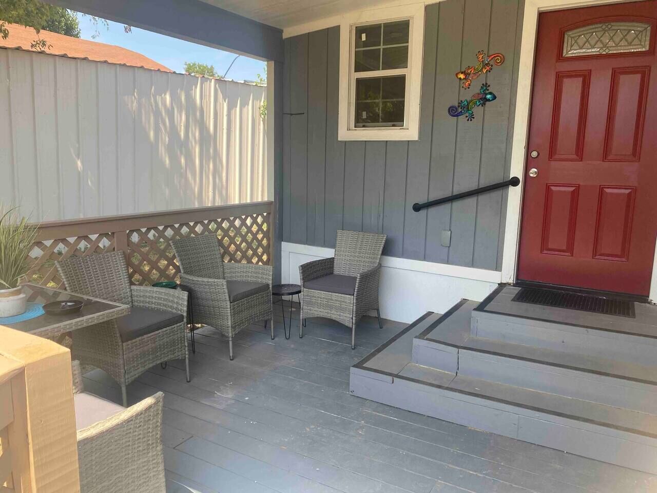 A covered porch with wicker furniture, a red door, and a small set of steps leading to the entrance.