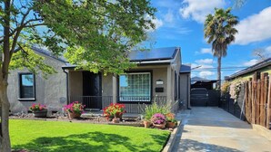 A residential house with a well-maintained lawn, potted plants, and a clear sky. - 2/1 Cozy Home in the Heart of the City (Stockton)