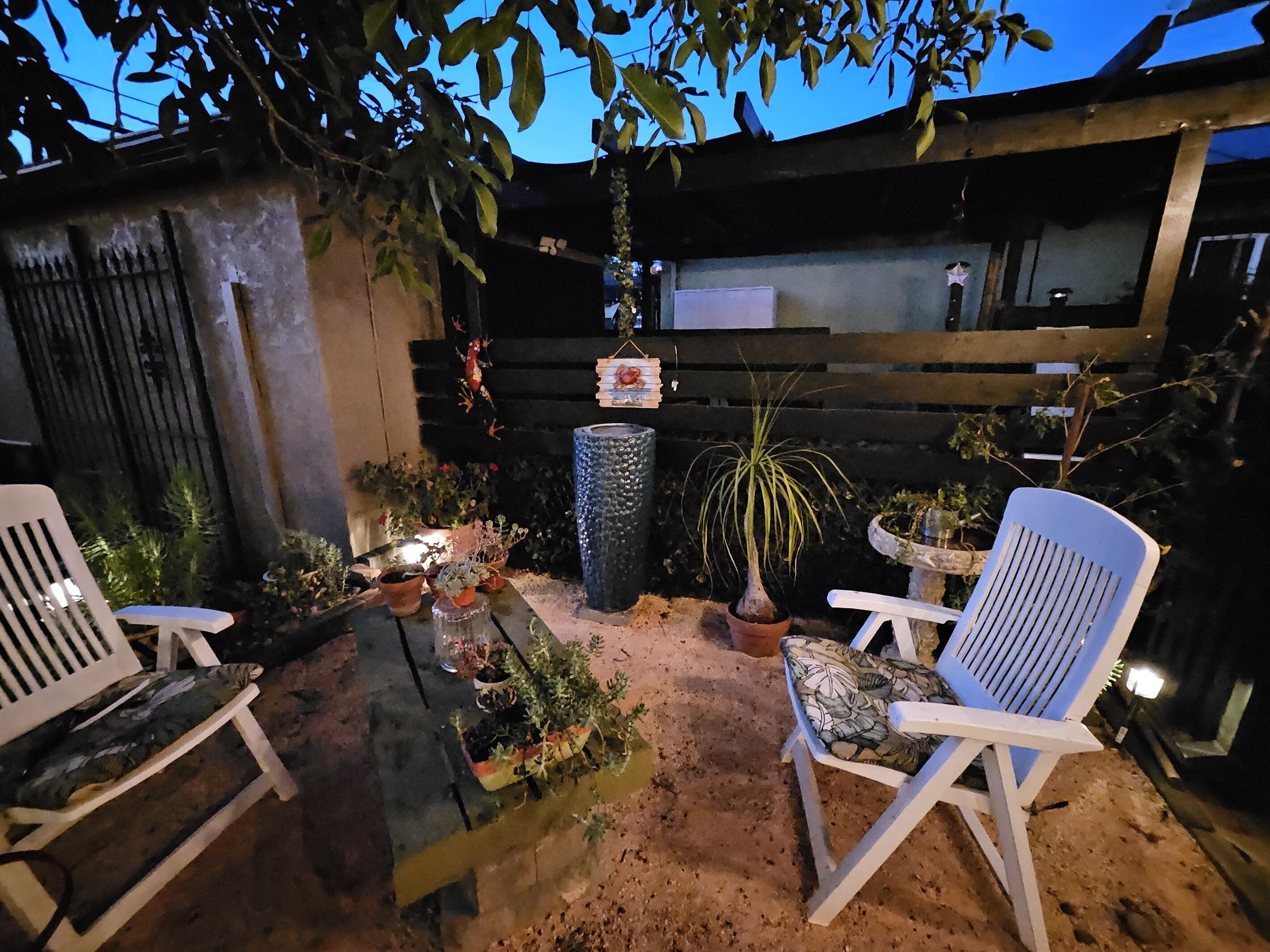 An outdoor seating area with two white chairs, a table, and various potted plants.