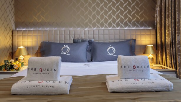 A hotel room with a large bed, two pillows with a crest logo, bedside lamps, and two towels with the hotel name. - Villa Vinicia 1 Deluxe Apartment (Luxembourg)