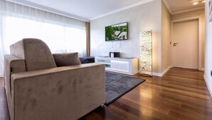 A modern living room with a sofa, a TV mounted on the wall, and a wooden floor. - Villa Vinicia 1 Deluxe Apartment (Luxembourg)