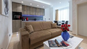 Un salon moderne avec un canapé beige, une table basse sur laquelle sont posés des magazines et un vase bleu contenant des fleurs rouges.