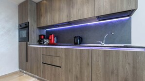 Une cuisine moderne dotée de meubles en bois, d’un plan de travail en acier inoxydable, d’un four encastré, d’une machine à café et d’une bouilloire.