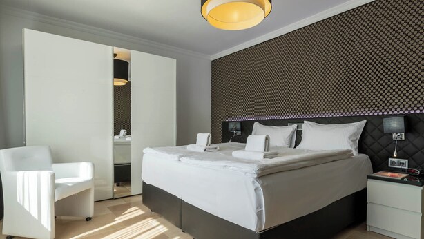 Une chambre d’hôtel moderne avec un grand lit, une chaise blanche, une table de chevet et un mur à motifs.