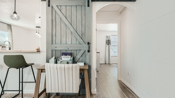 Una cocina con una puerta de madera rústica, una zona de comedor con mantel a rayas y una silla verde.