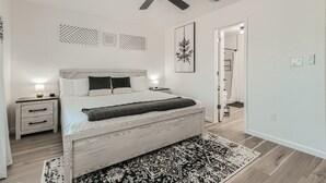 Un dormitorio con una cama de madera, mesitas de noche, ventilador de techo y alfombras estampadas.