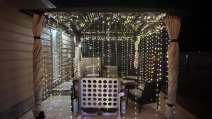 Un espacio de estar al aire libre techado, con luces colgantes, una mesa y sillas.