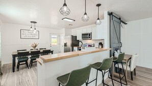 Una cocina moderna con armarios blancos, una isla central, taburetes de bar e iluminación colgante.