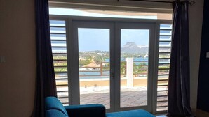 A room with a large sliding glass door leading to a balcony with a view of a beach and mountains. - Apartment, with pool near Jan Thiel Beach! 
 (Willemstad)