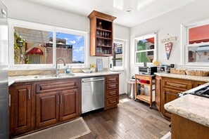 A modern kitchen with wooden cabinets, a stainless steel dishwasher, and a large window.