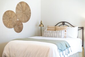 A bed with a white comforter, a green throw blanket, and patterned pillows.