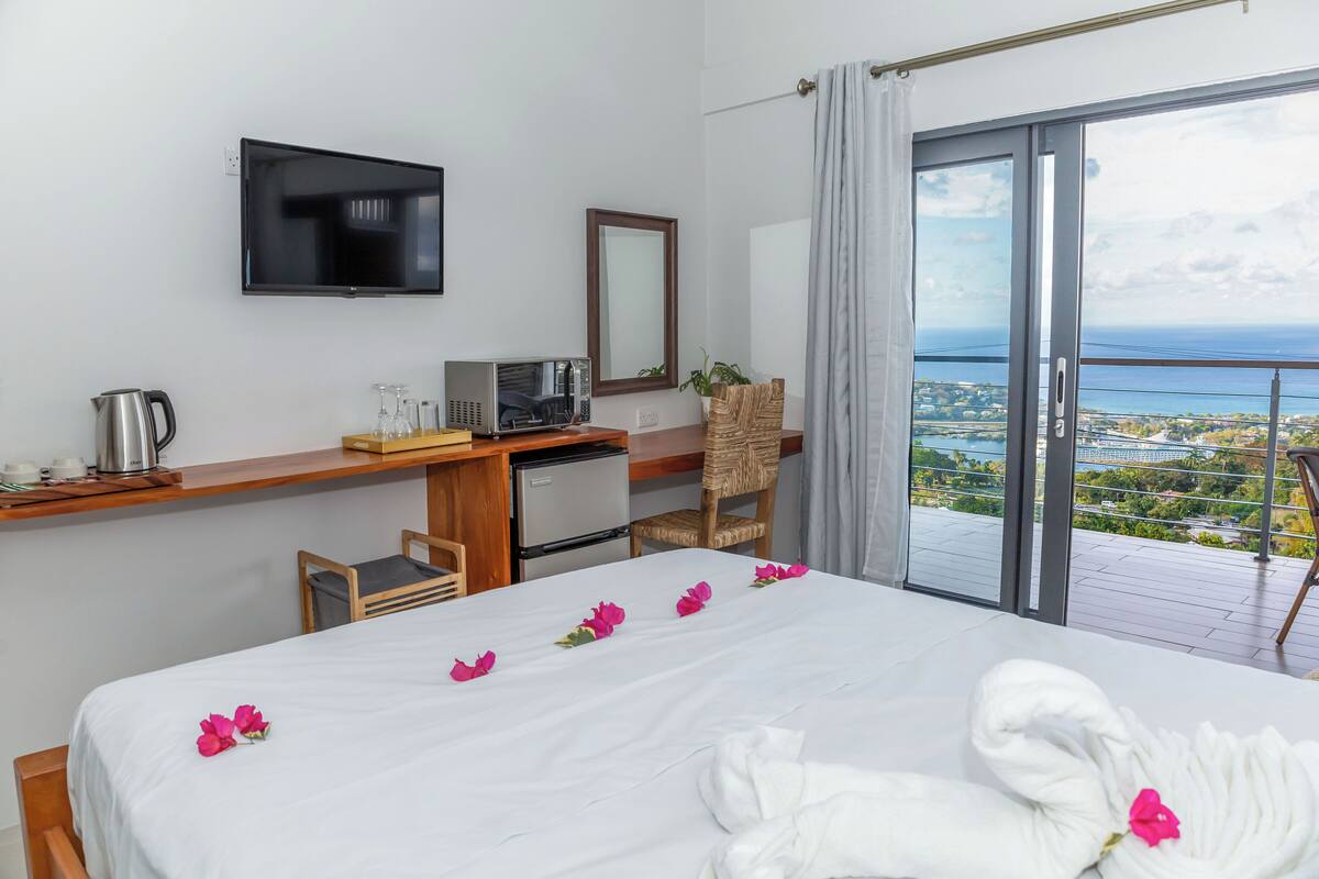 A hotel room with a bed, a desk with a computer, a television, and a balcony with a view.