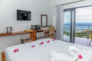 A hotel room with a bed, a desk with a computer, a television, and a balcony with a view.