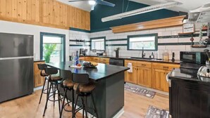 A modern kitchen with a central island, bar stools, wooden cabinets, and a ceiling fan. - Cozy Lake Retreat (Honeoye)