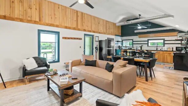A modern living room with a sofa, coffee table, and a dining area with chairs. - Cozy Lake Retreat (Honeoye)