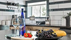 A kitchen with a window, a bottle, two glasses, a plate with grapes and a banana, and a strawberry. - Cozy Lake Retreat (Honeoye)