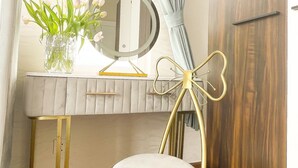 Un baño con tocador, espejo, silla y ventana con cortinas.