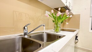 Una cocina moderna con dos fregaderos de acero inoxidable, encimera de mármol y un jarrón con flores rosadas.