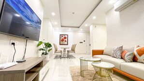 Una sala de estar moderna con un televisor de pantalla plana, una zona de comedor con mesa y sillas, un sofá con cojines y una planta en maceta.