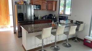 Une cuisine moderne dotée d’un plan de travail en granit, d’appareils électroménagers en acier inoxydable, d’armoires en bois et de tabourets de bar.