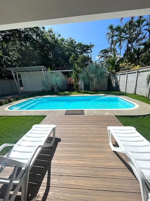 Une piscine avec une terrasse en bois et deux chaises longues blanches.