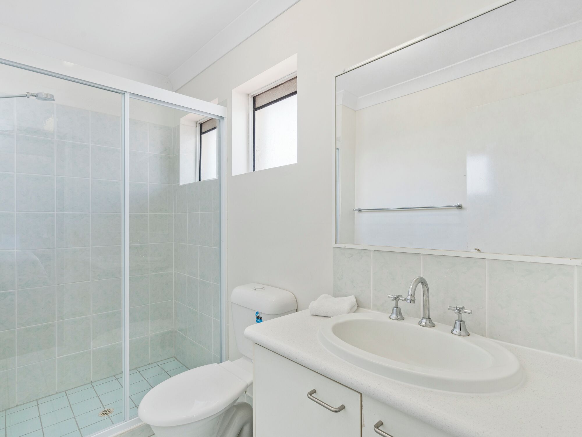 A modern bathroom with a glass shower enclosure, a white toilet, a sink with a mirror, and a towel rack.