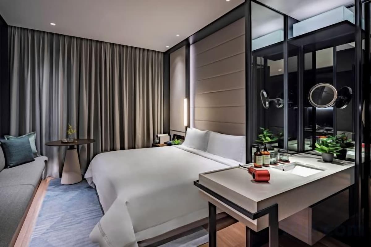 A modern hotel room with a large bed, bedside table, and a bathroom with a mirror and sink.
