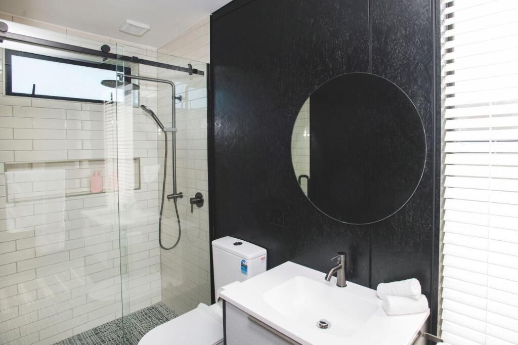 A modern bathroom with a glass-enclosed shower, a white sink with a mirror, and a black accent wall.