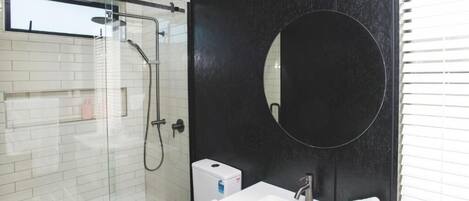 Un baño moderno con cabina de ducha de vidrio, un lavamanos blanco con espejo y una pared de acento negra.