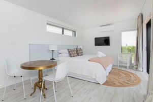 Un dormitorio moderno con cama, mesita de noche, sillas, una mesa redonda y un televisor.