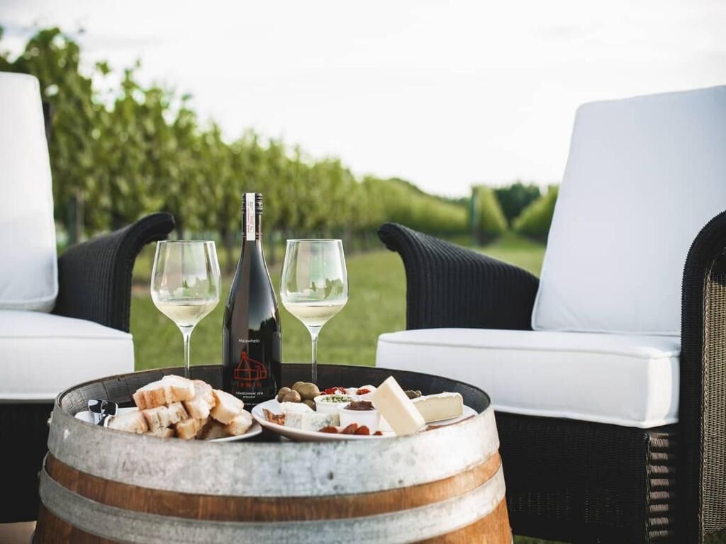 A dining setup with a wine bottle, glasses, and a plate of cheese and crackers on a barrel.