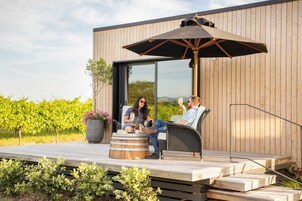 Una terraza de madera con dos sillas de mimbre, un paraguas grande y un barril de vino.
