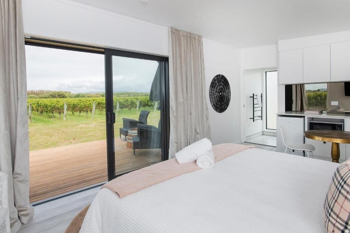 Un dormitorio con una cama grande, un escritorio y vistas a un viñedo a través de una puerta corrediza de vidrio.