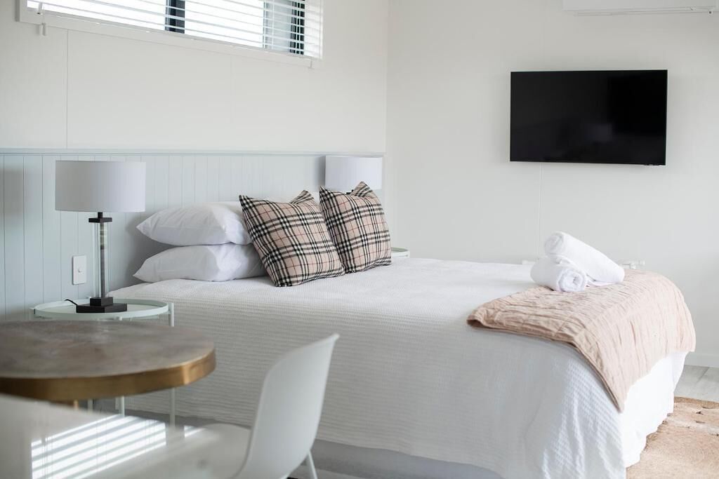 A hotel room with a bed, a TV mounted on the wall, a bedside table with a lamp, and a chair.