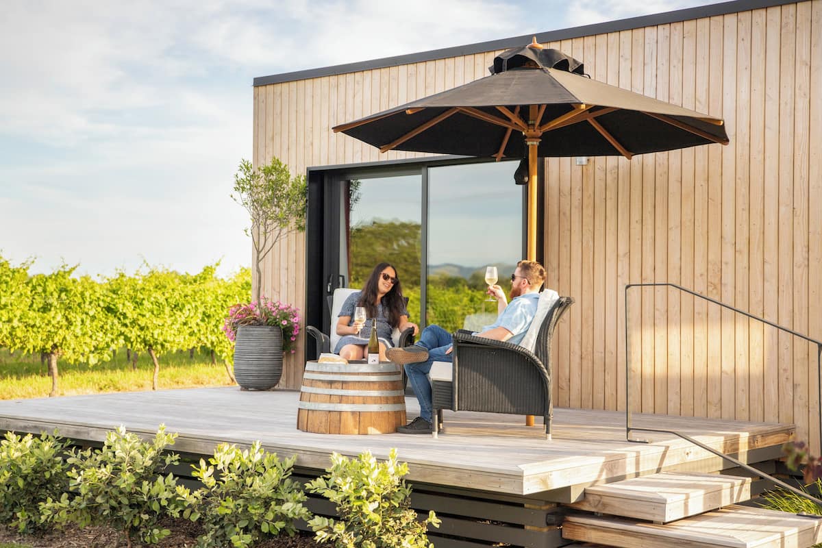 A wooden deck with two wicker chairs and a large umbrella, overlooking a vineyard.