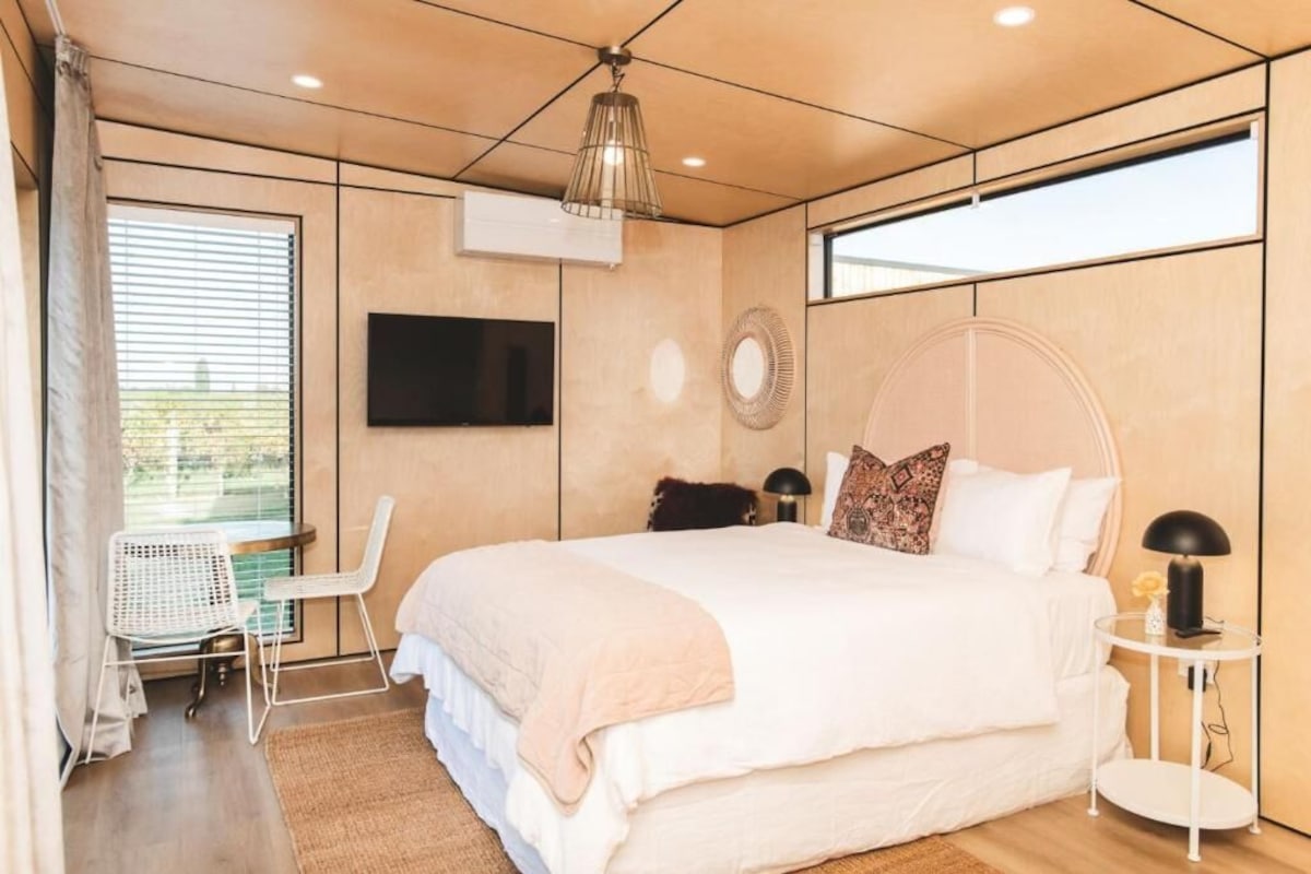 Un dormitorio moderno con una cama grande, un televisor en la pared y una ventana con persianas.