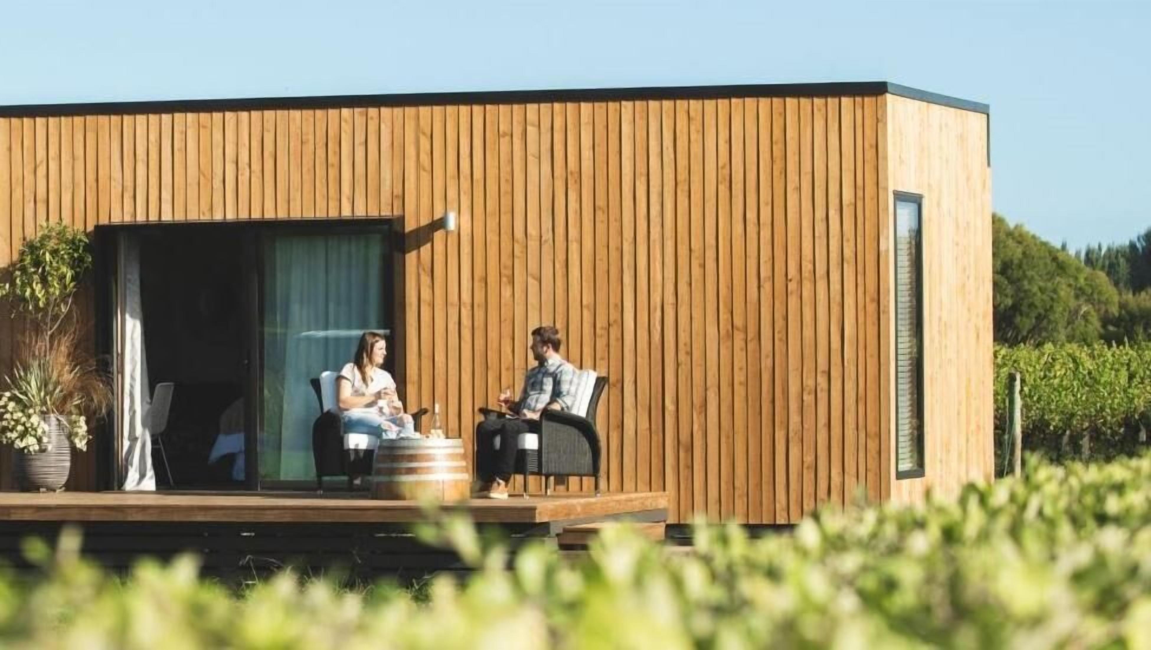 Una cabana de fusta moderna amb una porta corredissa de vidre, una zona d'seients exterior petita i vistes a la vegetació circumdant.