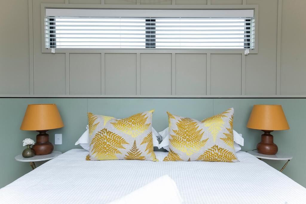 A hotel room with a bed, two bedside lamps, and a window with blinds.