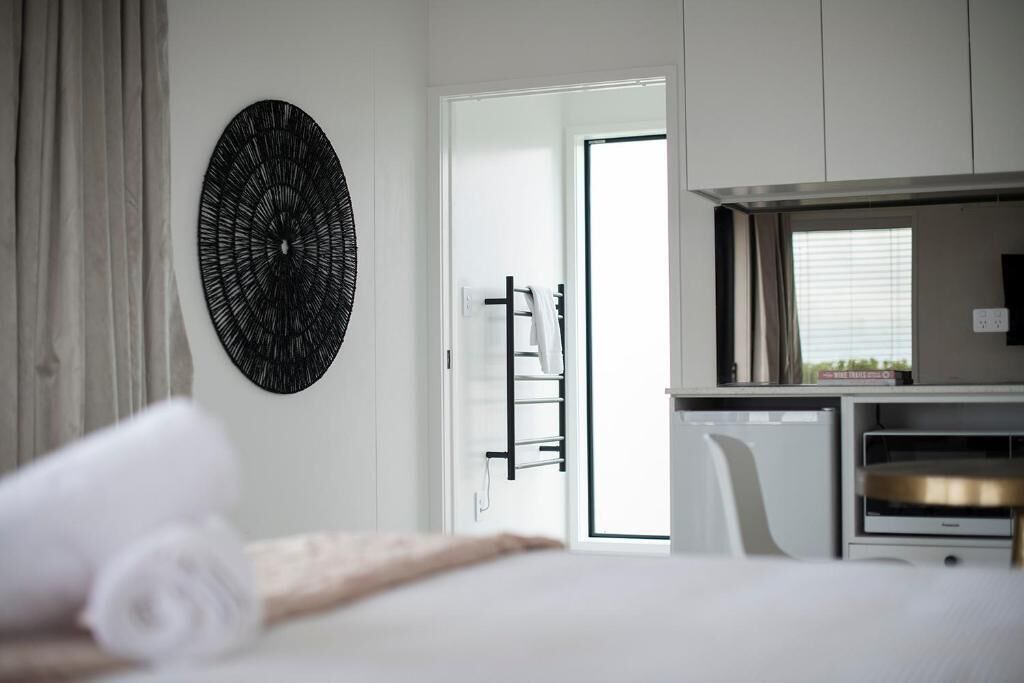 A hotel room with a bed, a wall-mounted artwork, a door leading to a bathroom, and a small kitchenette area.