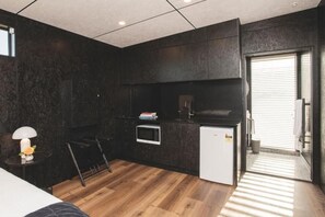 A compact kitchen with dark walls, a microwave, a small refrigerator, and a dining area with a chair and table.