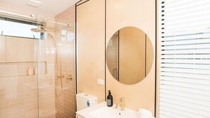 A modern bathroom with a glass-enclosed shower, a white sink with a gold faucet, and a large mirror. - Matawhero Wines  (Gisborne)