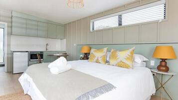 A bedroom with a large bed, bedside lamps, and a view of the kitchen.