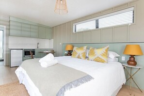 A bedroom with a large bed, bedside lamps, and a view of the kitchen.