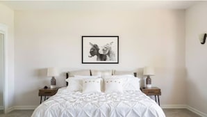 Een slaapkamer met een groot bed, twee nachtkastjes en een ingelijst kunstwerk aan de muur.