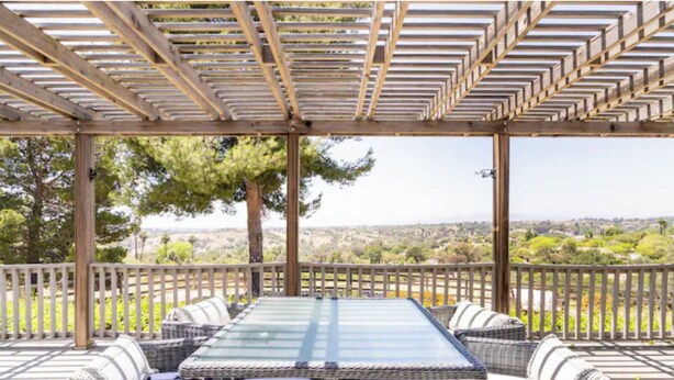 Een overdekt terras met een tafel en stoelen, omgeven door een houten balustrade, met uitzicht op een schilderachtig landschap.