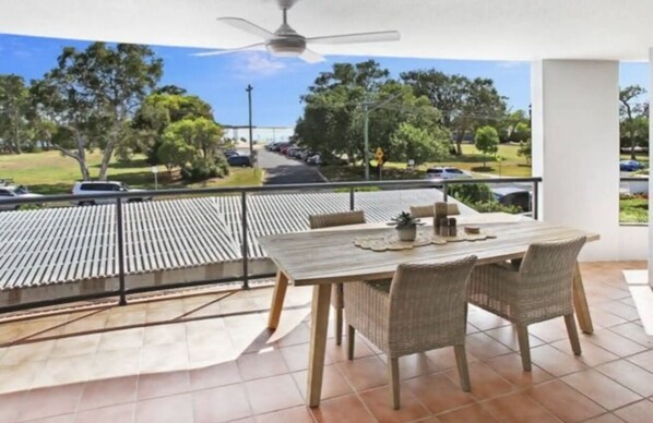 A balcony with a table and chairs, a ceiling fan, and a view of a road and greenery. - Absolute Waterfront (Maroochydore)