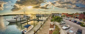 A marina with docked boats, a pedestrian walkway, and a parking area with cars.
